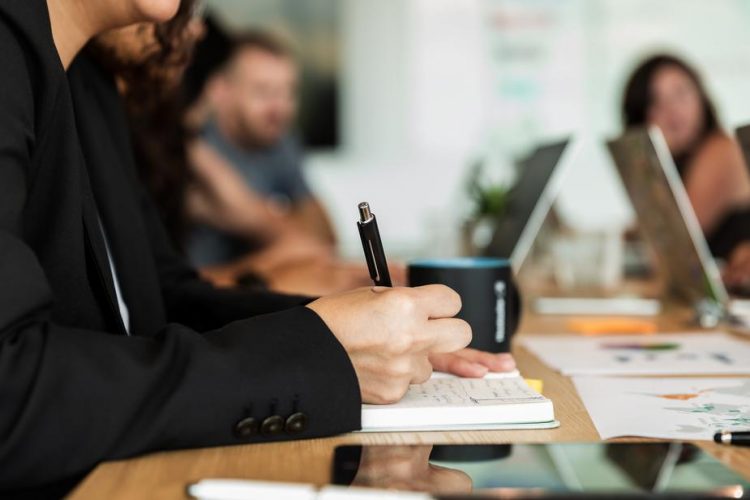 woman-writing-in-notebook-during-meeting