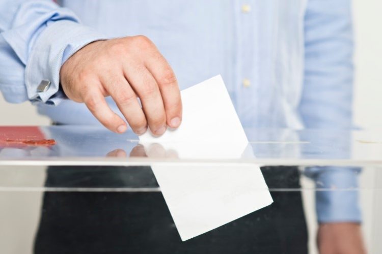 A person putting a ballot into a ballot box