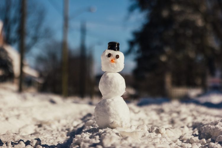 a snowman sits on a snowy lawn