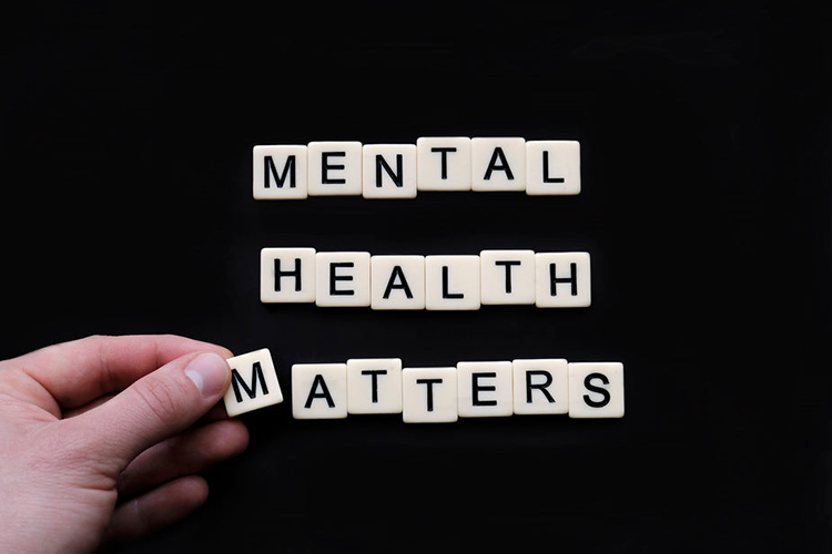 Scrabble tiles on a black background, with a hand holding one of the tiles. the tiles read Mental Health Matters